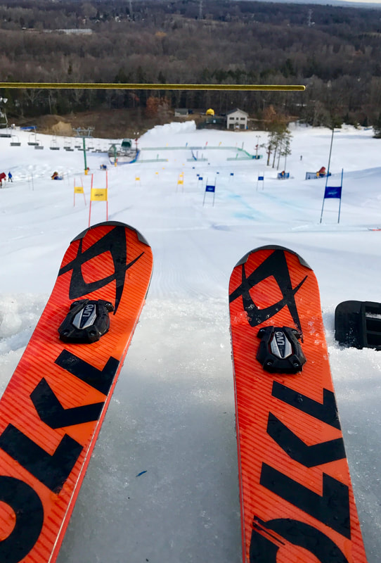 An image of orange skis at the top of a hill, waiting to push forward and about to race down a ski racing hill on snow.